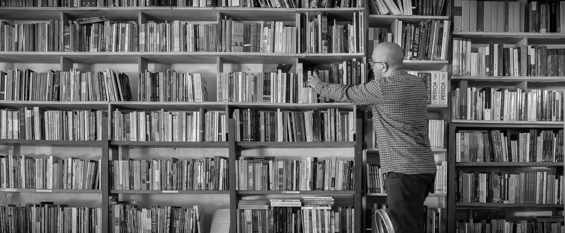 Bruno Eliezer, equilibrado em uma escada portátil, alcança um livro em uma das estantes mais altas da Livraria Ponta de Lança.